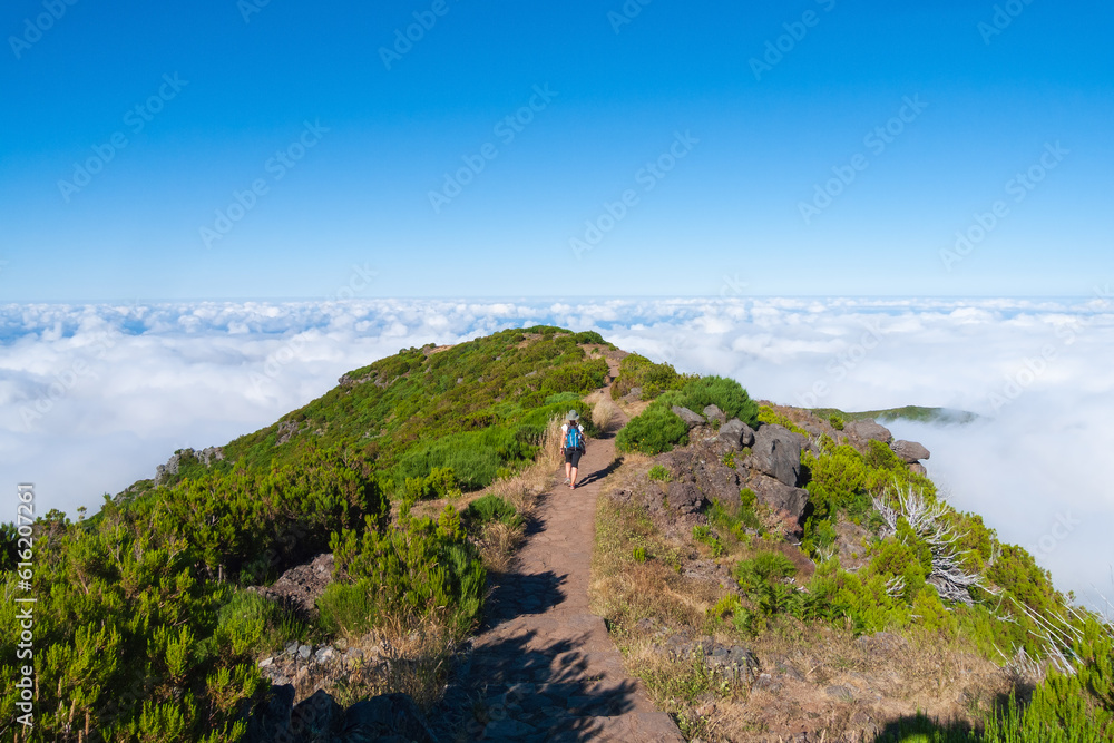 Una senderista sobre una montaña se dirige hacia un mar de nubes al horizonte en la isla de Madeira, Portugal.