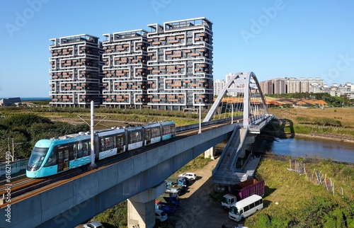 Aerial view of a metro train of Danhai Light Rail Transit traveling across a bridge with residential buildings standing under blue sunny sky in background, in Tamsui District, New Taipei City, Taiwan photo