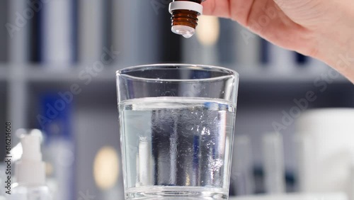 health care, woman drips drops from a bottle with a dispenser into a transparent glass of water to normalize pressure, close-up photo