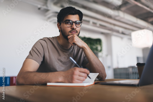 Thoughtful ethnic man writing in notepad at table