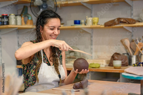 Young woman working raw ceramic and clay to make future ceramic product. Pottery workshop with natural light scraping, smoothing, shaping and sculpting. making clay pot