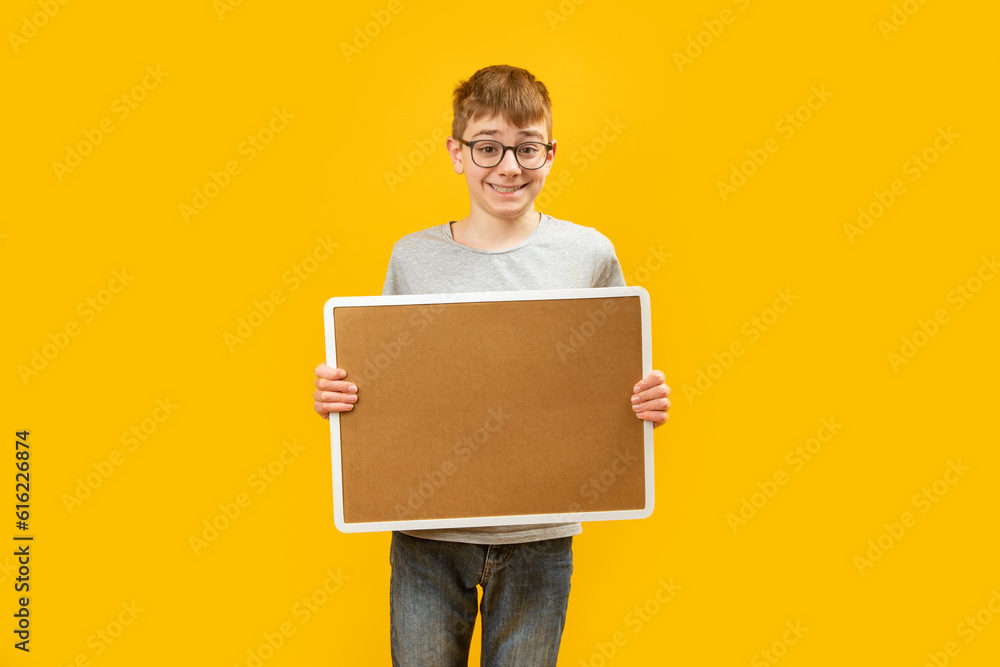 Teenage boy with glasses holding an empty cork board. Copy space. Mock up. High school student with blank board in his hands. Teenage boy with glasses holding an empty cork board. Copy space. Mock up. High school student with blank board in his hands.