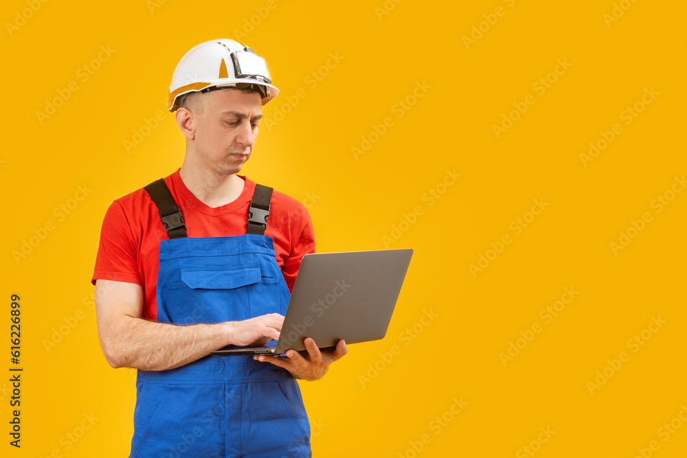 Male industrial engineer or worker standing with laptop on yellow background in photo studio. Copy space.