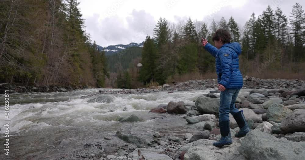 Young boy underhand throws a rock into a rushing river at base of mountains - nature adventure Young boy underhand throws a rock into a rushing river at base of mountains - nature adventure