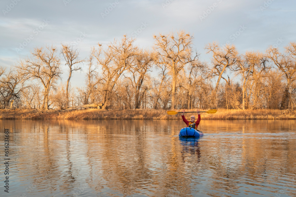 Fototapeta premium senior male is paddling an inflatable packraft on a calm lake with heron rookery in early spring in northern Colorado