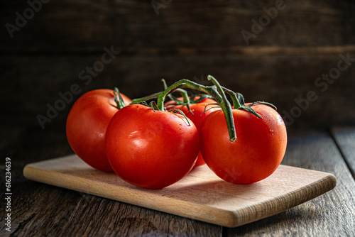 A branch of ripe tomatoes on a cutting board in the kitchen.