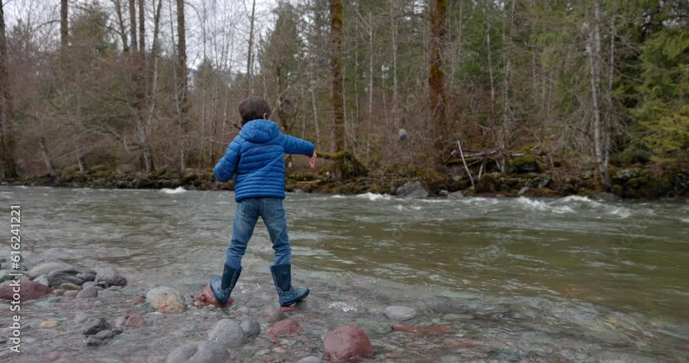 Young boy throwing rocks into river out in nature making big splash Young boy throwing rocks into river out in nature making big splash