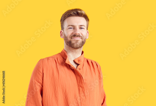 Confident smiling young redhead bearded handsome man wearing casual bright orange summer shirt isolated on studio yellow background. Smart guy looking at the camera. People portrait concept.