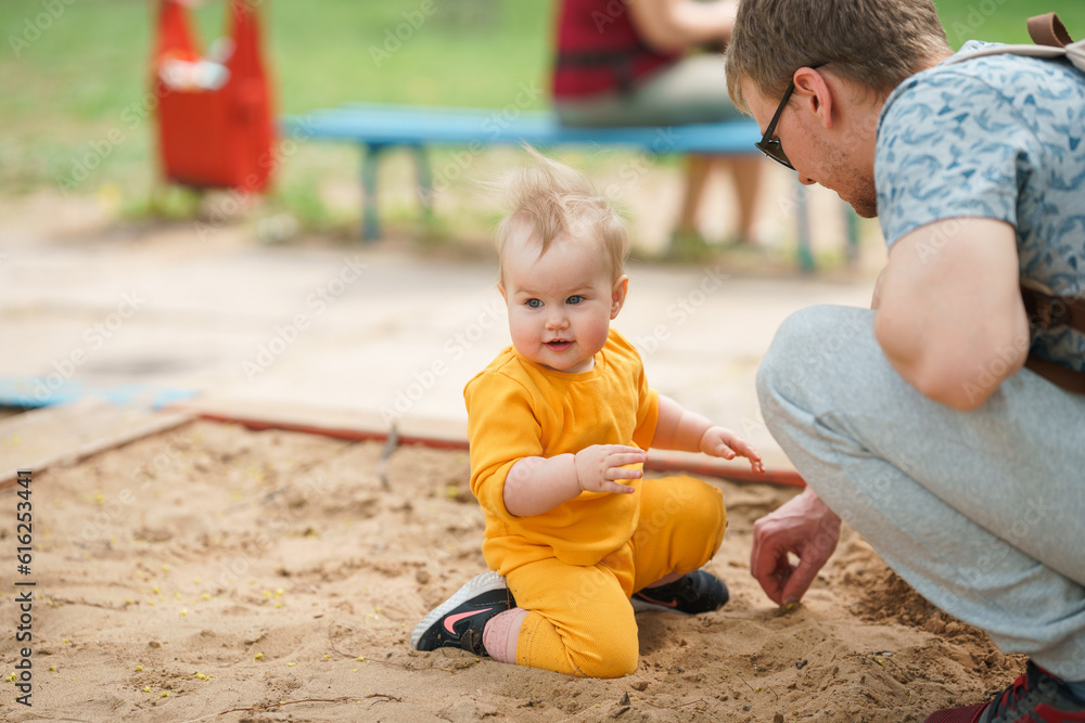 Blonde toddler plays on the playground in the sandbox with his dad Blonde toddler plays on the playground in the sandbox with his dad