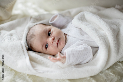 Newborn baby lying covered with white blanket.