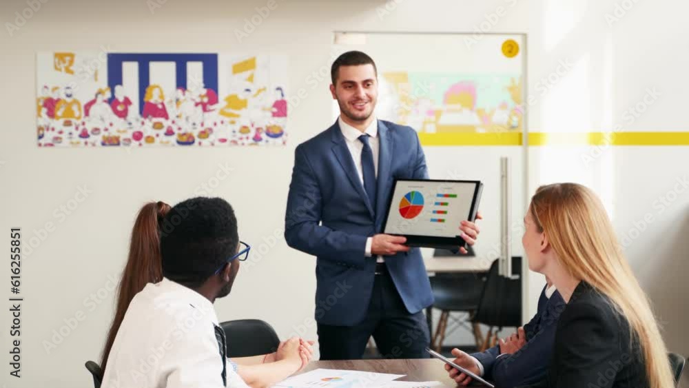 Businessman presents report, shows diagrams on tablet pc in conference room for multiethnic partners. Diverse international team listen CEO on board meeting in office. Corporate people discuss plan. Businessman presents report, shows diagrams on tablet pc in conference room for multiethnic partners. Diverse international team listen CEO on board meeting in office. Corporate people discuss plan.