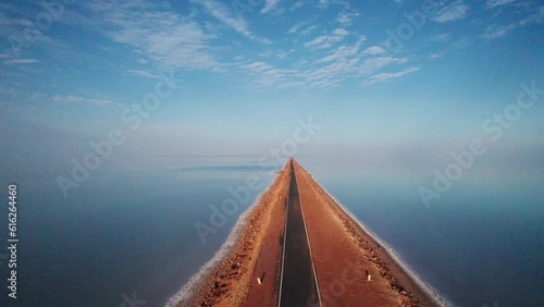 4K aerial view of beautiful road and salt water lake on both sides, connecting Khavda to Dholavira in Kutch, Gujarat, India. Road to heaven. Road trip. Clouds in sky with infinite road. photo