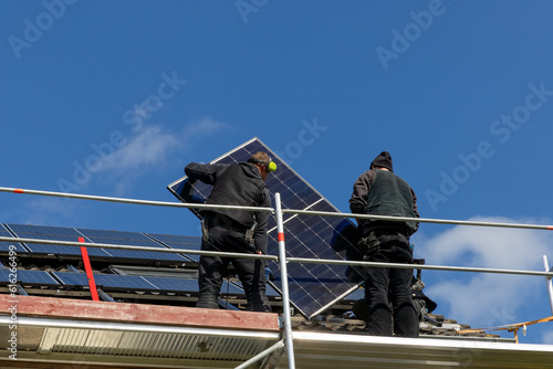 Craftsmen install a new photovoltaic system on a roof under a blue sky