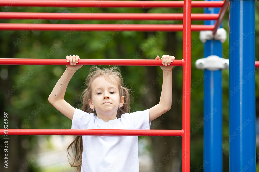 Obraz premium A cute little girl is engaged in sports simulators at the sport ground outdoors. Healthy lifestyle