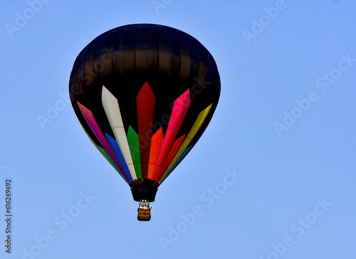 A View of a Hot Air Balloon  Black with Colored Stripes Flying in an all Blue Sky  in Early Fall