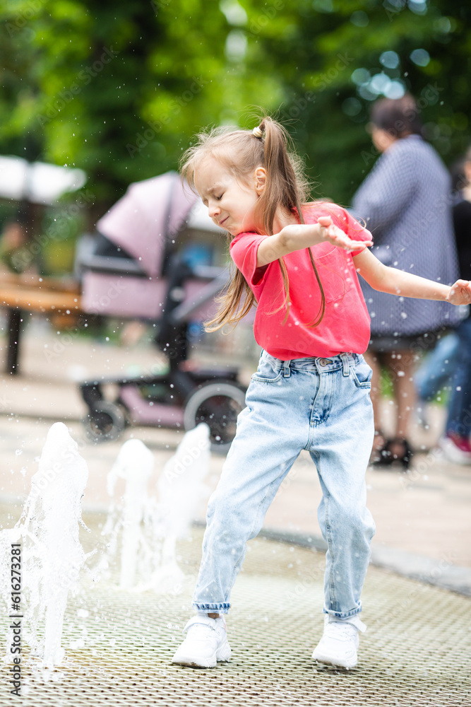 Naklejka premium Happy little toddler girl running through a fountain having fun with water splashes, enjoying summer family vacation