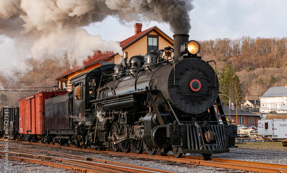 Obraz premium View of a Restored, Antique Steam Freight Train Approaching in Early Morning, on old Narrow Gauge Tracks on a Winter Day, Blowing Smoke