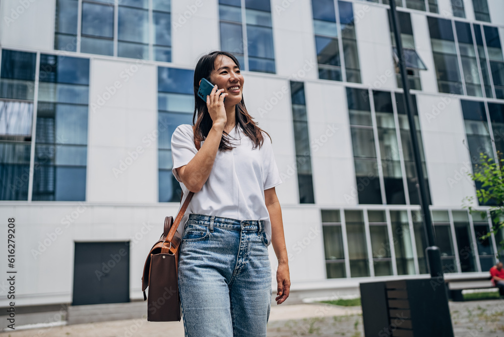 Fototapeta premium Young busy successful beautiful Japanese business woman, Japanese professional businesswoman holding cellphone using smartphone standing or walking on big city urban street outside