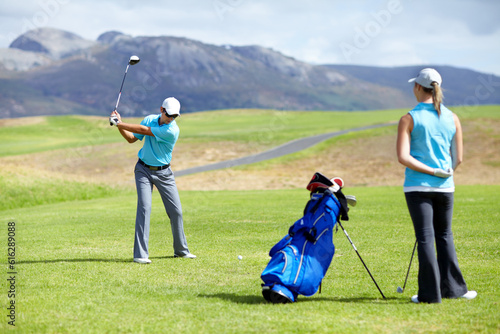 Swing, man or golfer playing golf for fitness, workout or exercise to drive on a green course. Woman, person golfing or athlete training in action or sports game driving with a club stroke on field