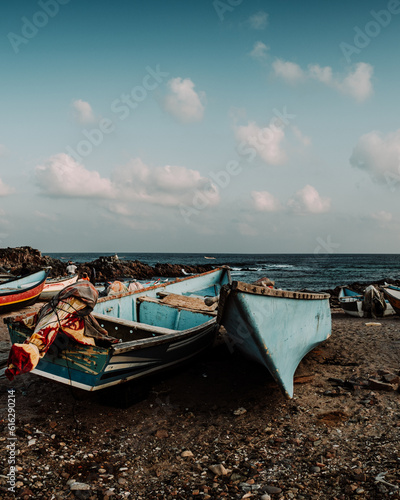 Fishing boats resting on the shore of Arher Beach in Socotra, Yemen, with the ocean and a partly cloudy sky in the background.