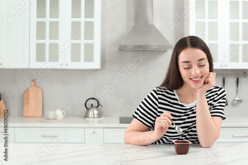Happy woman with tasty yogurt in kitchen. Space for text