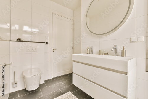 a white bathroom with black tile flooring and a round mirror on the wall above the sink is an oval shaped mirror