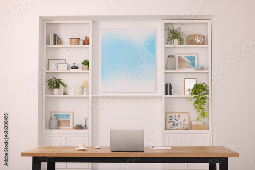 Interior design. Cosy workplace with laptop on wooden table near abstract picture between shelves