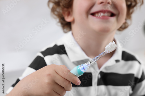 Little boy holding electric toothbrush indoors, closeup