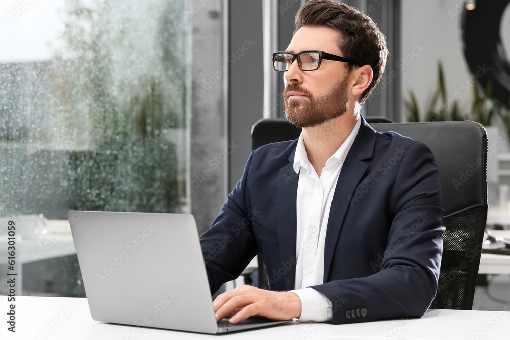 Man working on laptop at white desk in office Man working on laptop at white desk in office