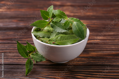 Fresh green bay leaves in bowl on wooden table