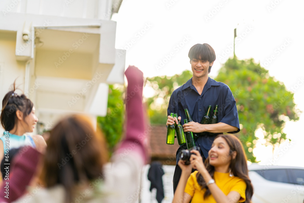 Obraz premium Group of Happy young Asian man and woman friends enjoy and fun reunion meeting party at home backyard with playing guitar, singing, eating food and drinking beer together on summer holiday vacation.