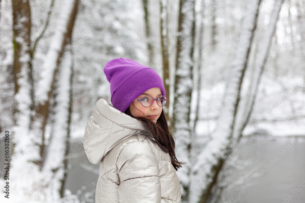 Fototapeta premium Portrait of a beautiful girl in a pink hat and glasses in the winter forest