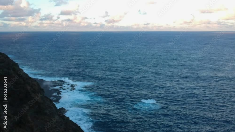 Aerial drone view of a seashore cliff with waves breaking on rocks close to the coastline at sunset in Oahu, Hawaii