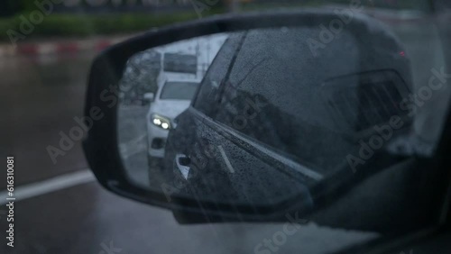 close up side rareview mirror of driving car on road in the evening and rainy day, slow motion scene photo