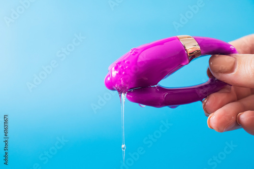 Billede på lærred A woman holds a curved sex toy in lubrication on a blue background