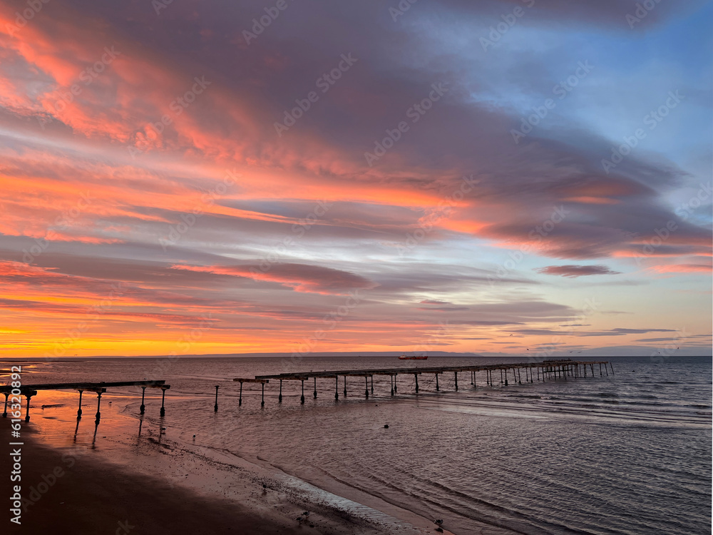 Huge colourful panoramic view at sunrise of the Costanera walkway with red and orange lenticular clouds in Punta Arenas, Chile Huge colourful panoramic view at sunrise of the Costanera walkway with red and orange lenticular clouds in Punta Arenas, Chile