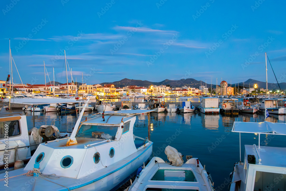 Evening view of the boats in the harbor port and the illuminated seaside village shops and cafes on the Saronic island of Aegina, Greece.	
