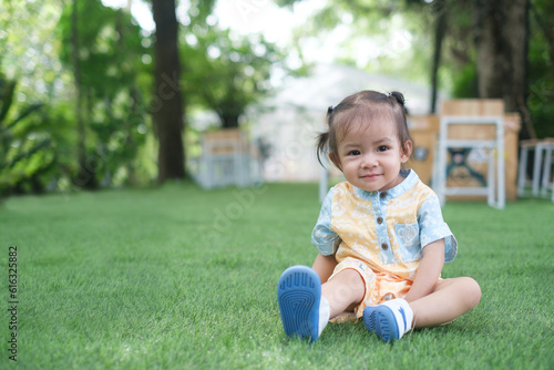Happy Baby Girl Smiling and Relaxing Enjoying Sunny Day on Green Grass under the Serene Tree - Joyful Toddler Enjoying Nature Outdoors.