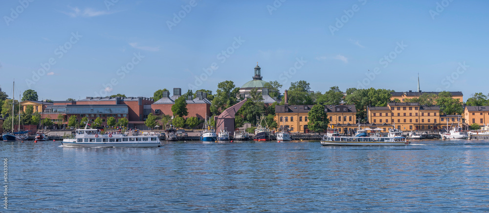 Inner harbor passenger ferry and tourist boat in the bay Ladugårdslandsviken, boats and old maritime buildings on the island Skeppsholmen, a sunny summer day in Stockholm