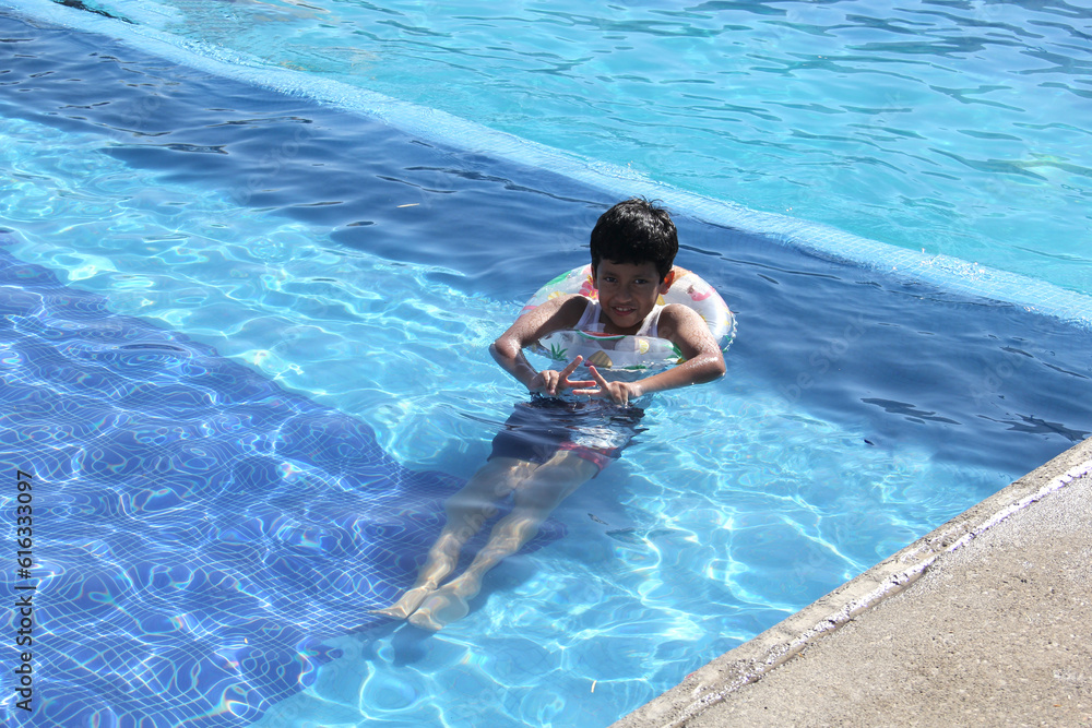 9-year-old brown-haired Latino boy swims in the pool, plays and enjoys his vacation under the sun with sunscreen