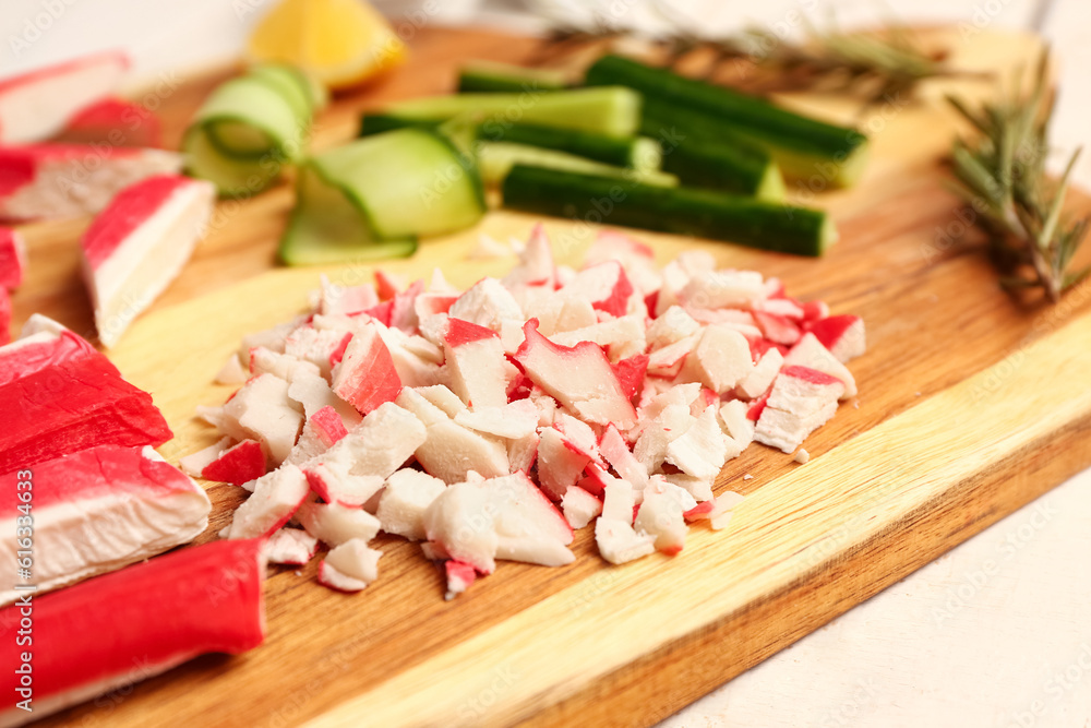 Wooden board with tasty chopped crab sticks on table, closeup