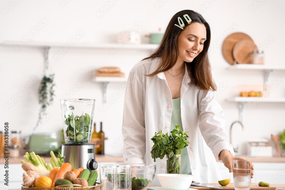 Young woman making vegetable juice in kitchen