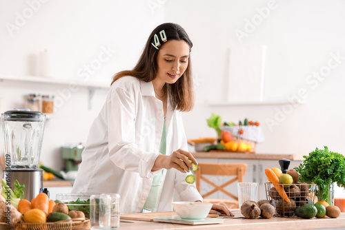 Young woman measuring cucumber slices on scales in kitchen
