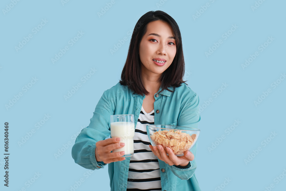 Young Asian woman with milk and cornflakes on light blue background Young Asian woman with milk and cornflakes on light blue background