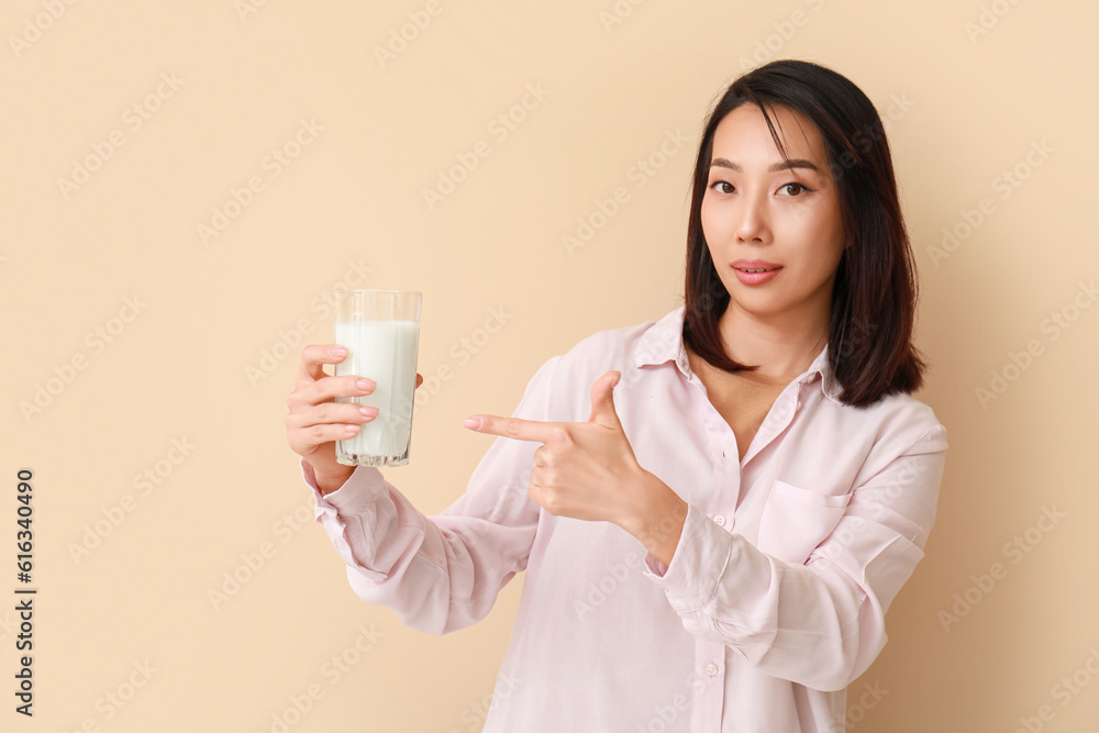 Beautiful Asian woman with glass of milk on beige background Beautiful Asian woman with glass of milk on beige background