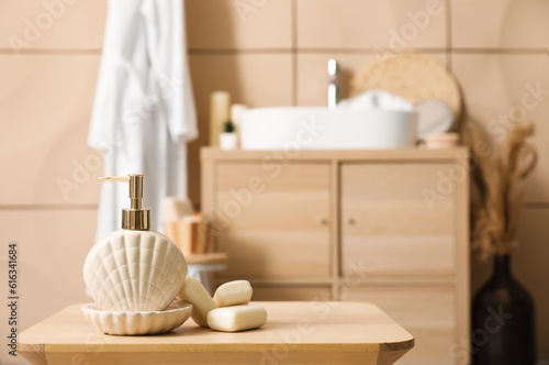 Soap dispenser and bars on wooden table in bathroom, closeup