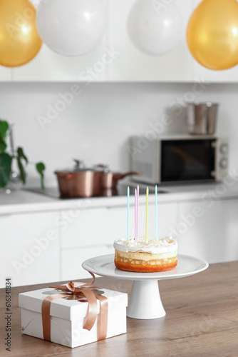 Stand with Birthday cake and gift on table in kitchen