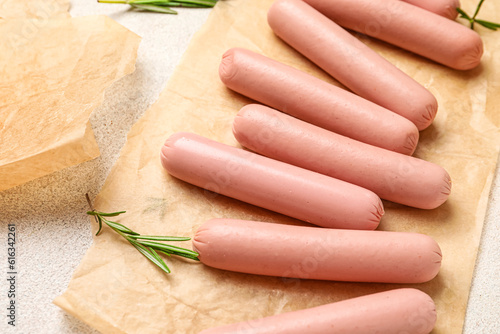 Baking paper with tasty thin sausages and rosemary on white background
