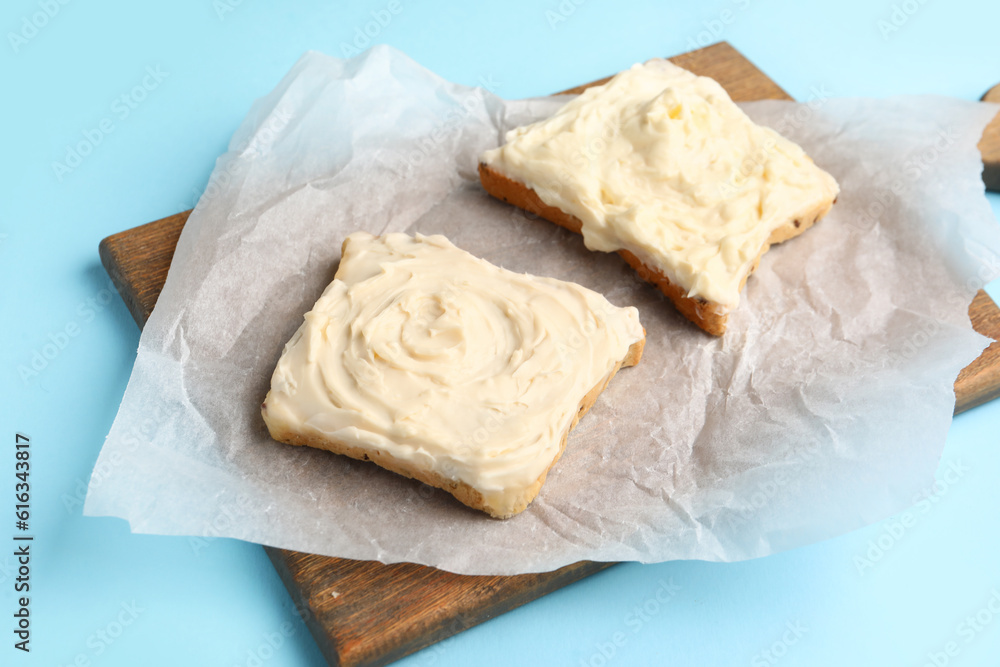 Wooden board of tasty toasts with cream cheese on blue background Wooden board of tasty toasts with cream cheese on blue background