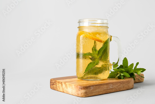 Board with mason jar of ice tea and lemon on white background
